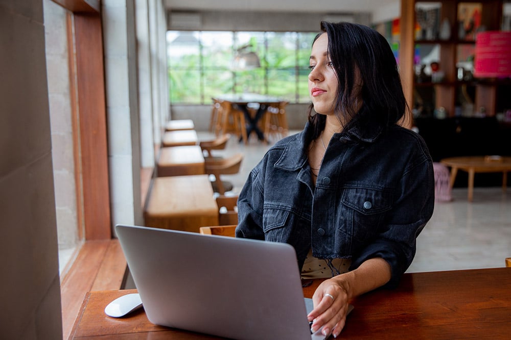 Woman at a table with a laptop looking out a window